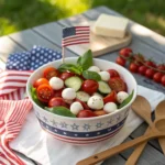 Flag-themed tablescape with cucumber tomato salad, mozzarella balls, and basil in a festive bowl, surrounded by patriotic decor and a red-white-blue napkin.