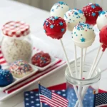 Red, white, and blue cake pops decorated with sprinkles and candy drizzle, displayed in a festive 4th of July-themed container with small American flags.
