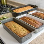 Side-by-side loaf pans with baked zucchini bread inside, labeled by material type: metal, ceramic, glass, and silicone.