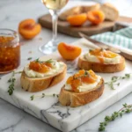 Toasted crostini with melted brie and glossy apricot jam, styled on a marble board with thyme garnish.