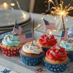Patriotic sparkler cupcakes with red, white, and blue frosting swirls, glittery sprinkles, and metallic sparkler toppers, displayed on a decorated 4th of July party table.