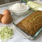 Beginner-friendly zucchini bread in a clear glass loaf pan with ingredients measured nearby.