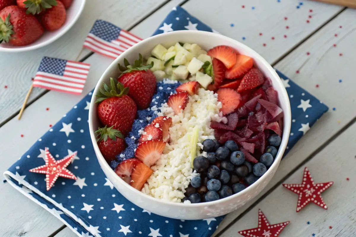 Red, white, and blue rice bowl with tomatoes, blueberries, feta, and herbs arranged in a patriotic design for 4th of July, served in a white bowl with festive decorations.