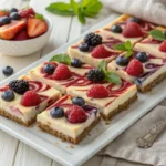 Creamy berry cheesecake bars with a golden graham cracker crust and vibrant swirls of raspberry and blueberry, served on a plate with fresh berries and mint garnish.