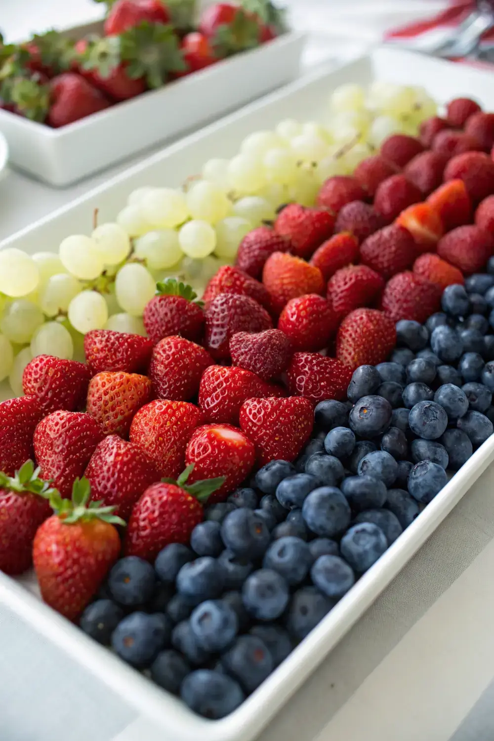 A colorful fruit tray featuring red strawberries, white grapes, and blue blueberries arranged in a patriotic pattern for an easy, alcohol‑free party snack.